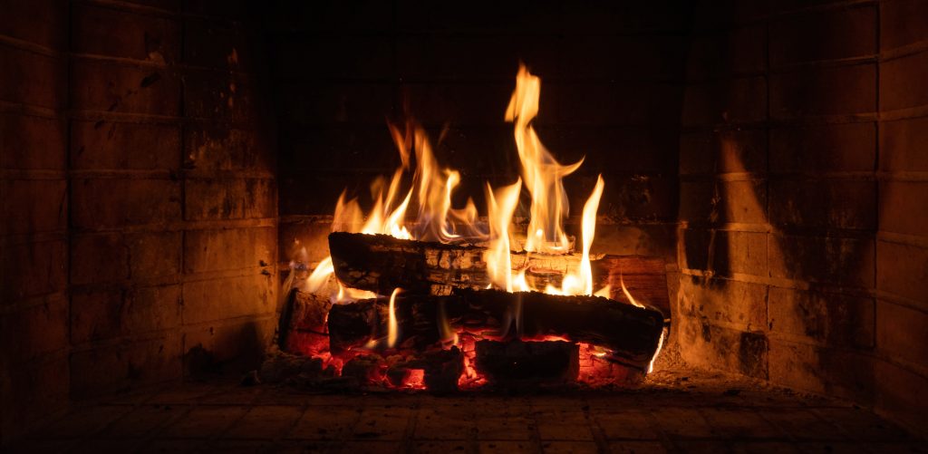 Fire burning in a fireplace wood logs and flames Warm home heat Christmas holiday - Spark Chimney LLC Cozy fireplace with burning logs and bright orange flames in a brick hearth.
